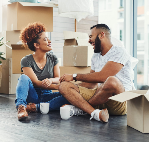 A couple sitting on the floor with cardboard moving boxes all around them