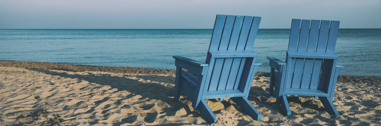 Two blue adirondack chairs on a beach