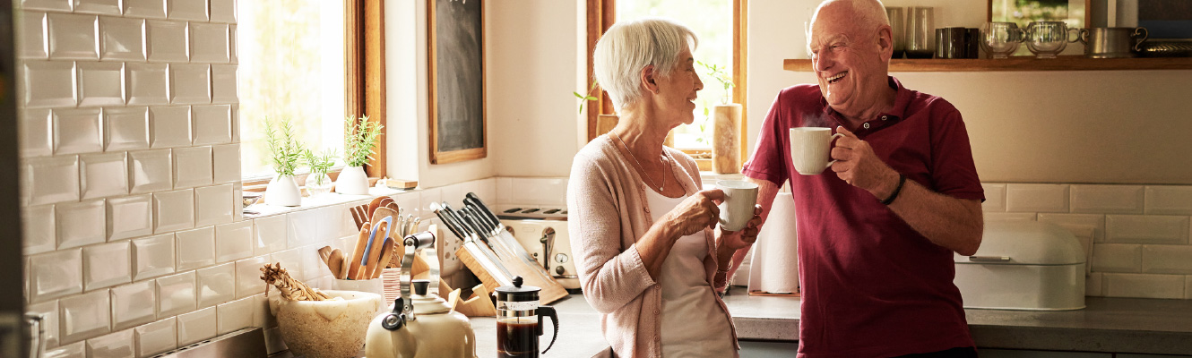 An older couple standing in a kitchen holding coffee cups