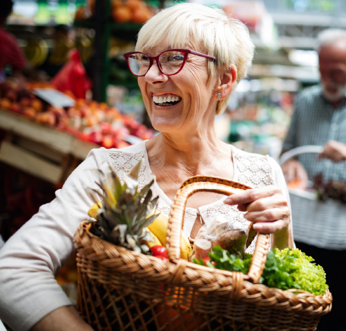 An older woman carrying a basket of fruits and vegitables