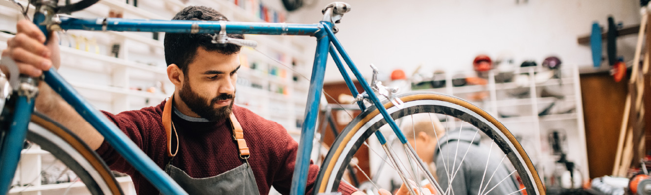 A man in a work apron holding a bicycle
