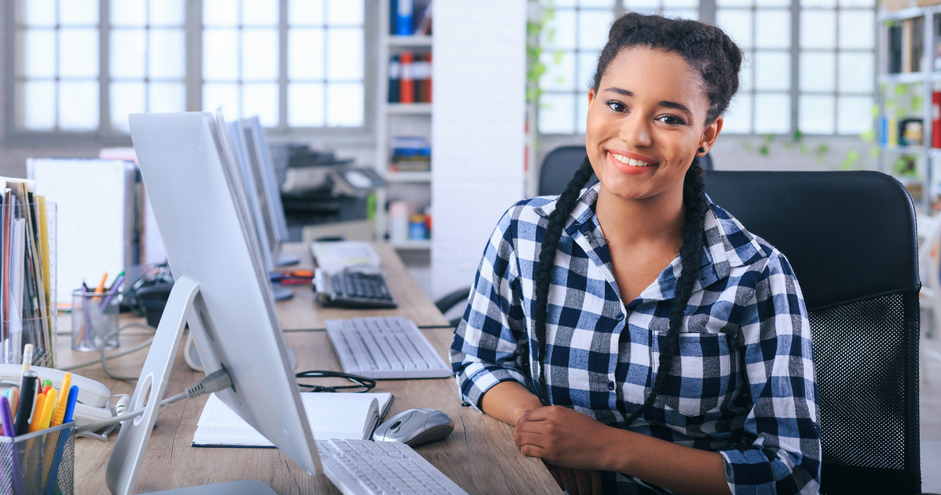 Woman witting at a office computer, smiling at the camera. 