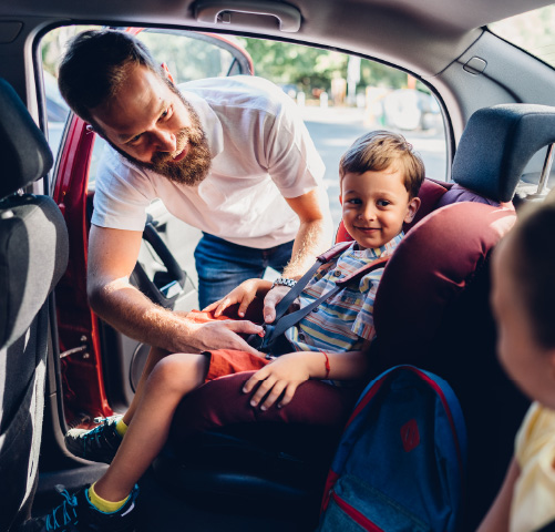 A dad helping two young children in the back of a car