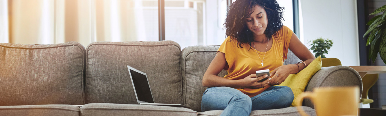 A young woman sitting on a long couch, she is looking at a phone