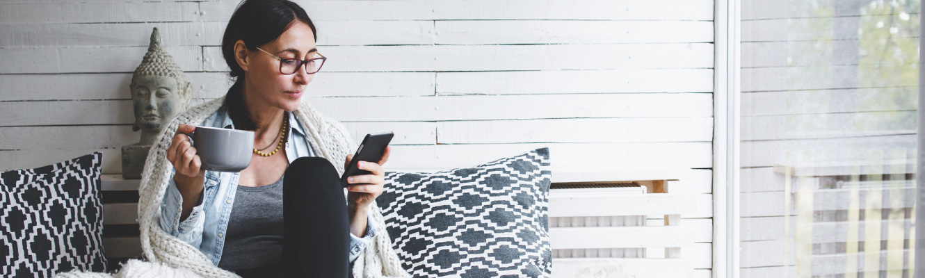 A woman sitting down holding a coffee cup and a smart phone