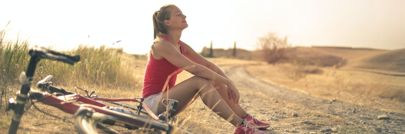 Athletic Woman Sitting Beside a Bike on a Dirt Road