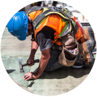 Construction worker hammering a nail. Bright orange vest and hunched down.