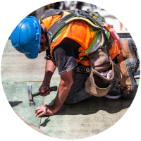 Construction worker hammering a nail. Bright orange vest  and hunched down. 