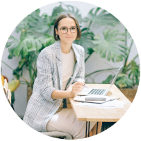 Person sitting at a table with a laptop. Looking into the camera. 