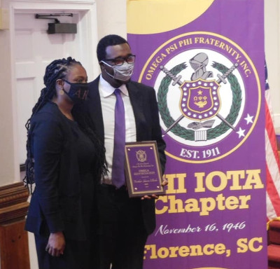 Shawn Ellerbe Posing with Award Next to Purple Banner