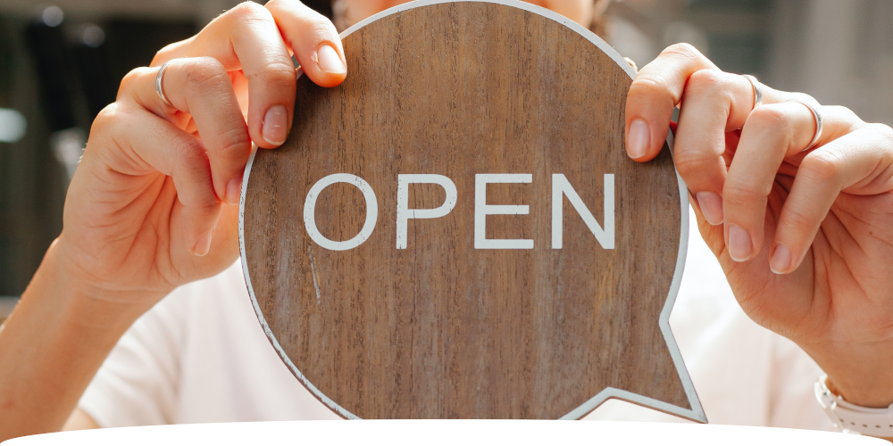 Wooden "OPEN" business sign in front of store owner. Close up shot.