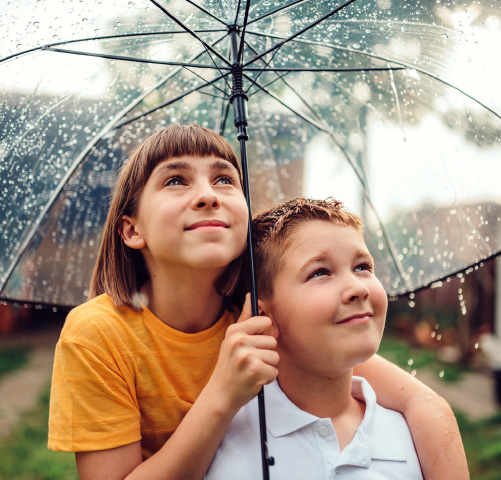 Two kids standing under an umbrella on a rainy day
