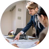 Person standing and pointing at a piece of  paper on a desk during a office meeting.