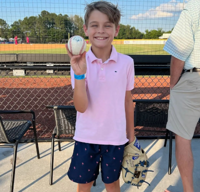 Child with baseball smiling. Pink shirt. At Carolina Bank Field.